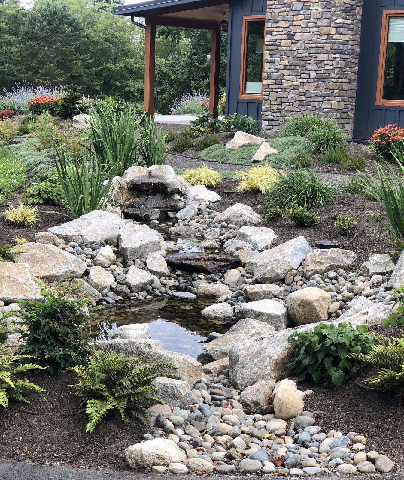 Cascading garden stream framed by stone, ferns, and ornamental grasses